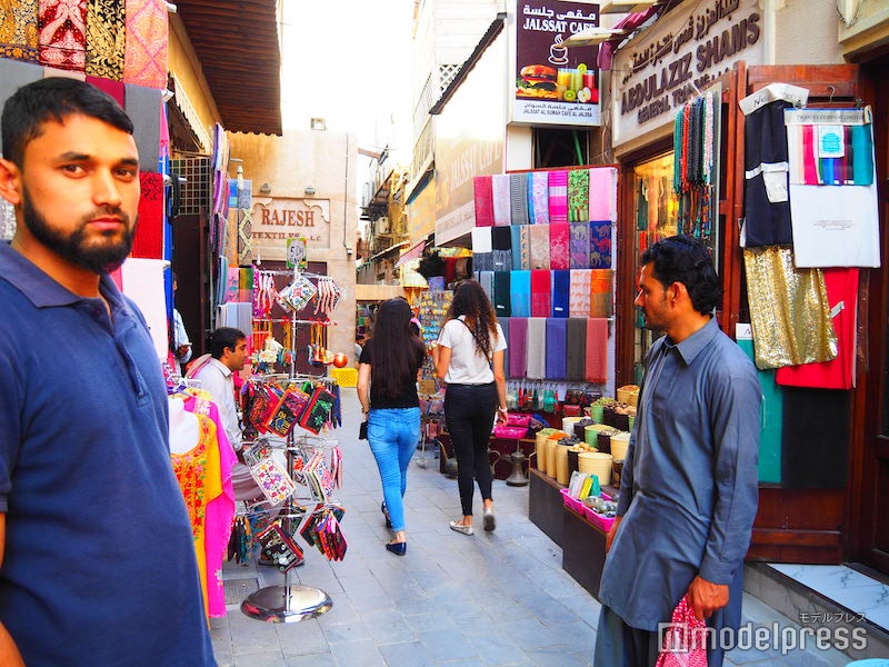 たくさんの店の前に商人が立っていて、客引きをしている（C）モデルプレス