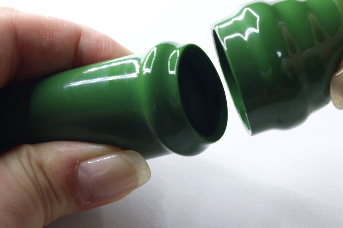 女性の手が緑色の小物入れキーホルダーを上下に開けている様子。内部の構造が見える