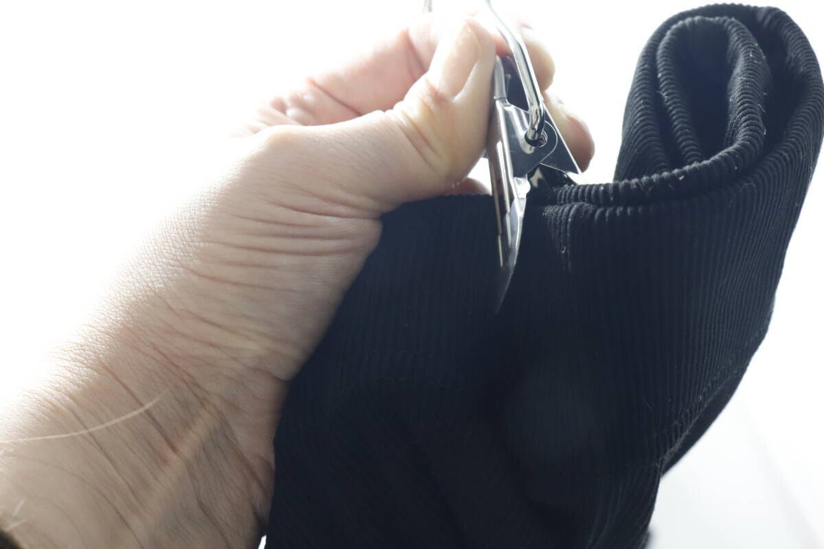 手でダイソーのフックピンチを使い、黒い衣類を挟んでいる様子