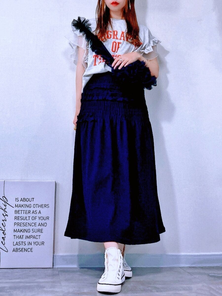 ロゴTと黒スカートを着た女性が黒いバッグを持ち立つ