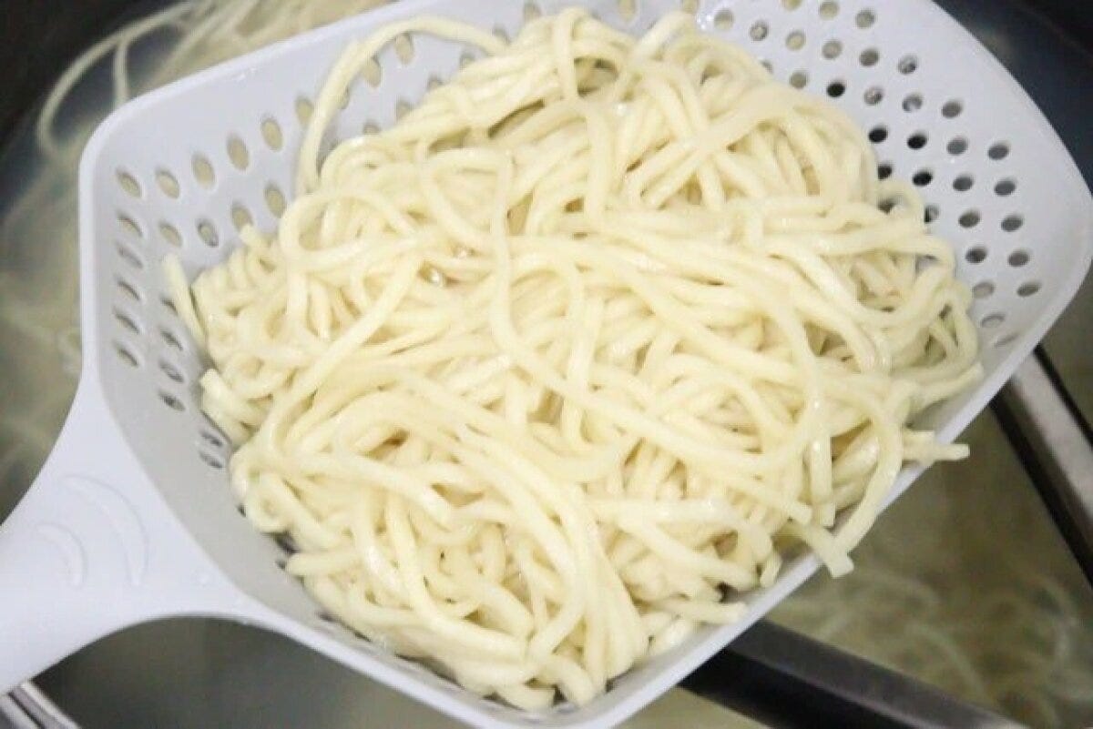 グレーのザルスプーンで鍋から茹でた麺をすくい上げている グレーのザルスプーンで鍋から茹でた麺をすくい上げている
