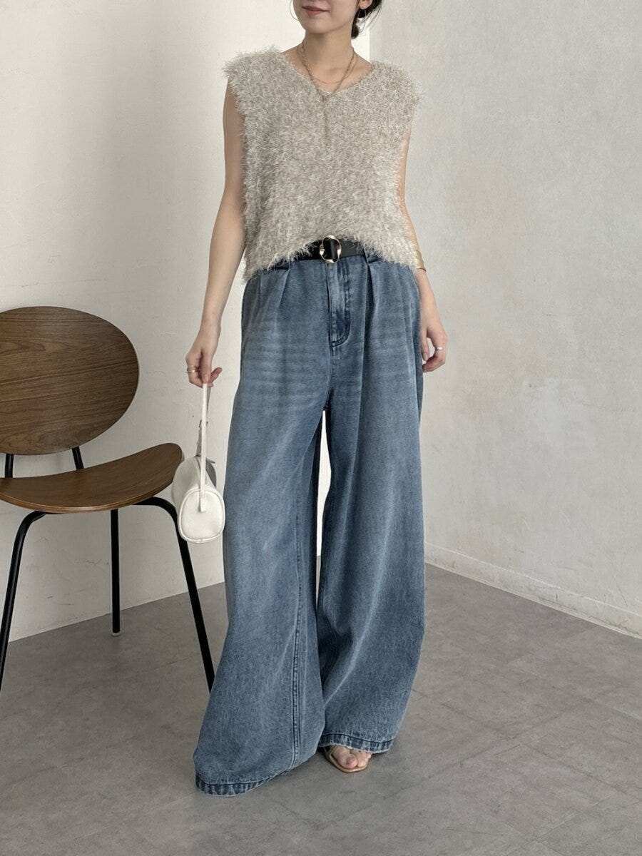 ベージュのシャギーニットベストとワイドデニムを着用し白いバッグを持つ女性