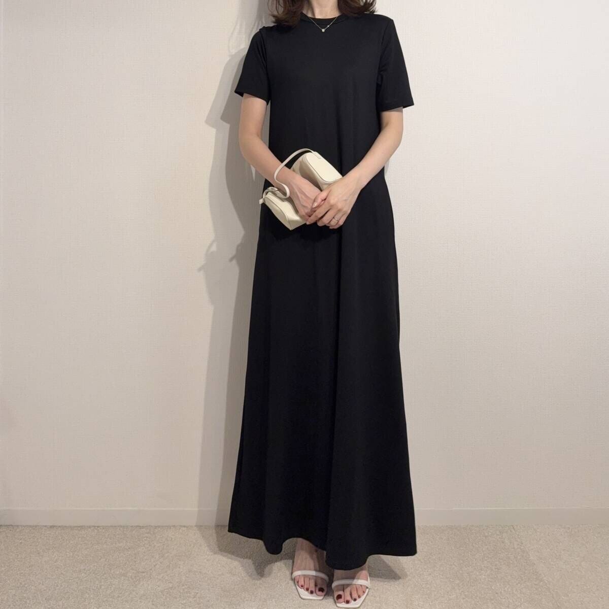 黒いワンピースに白いミニバッグとヒールサンダルを合わせた女性の全身