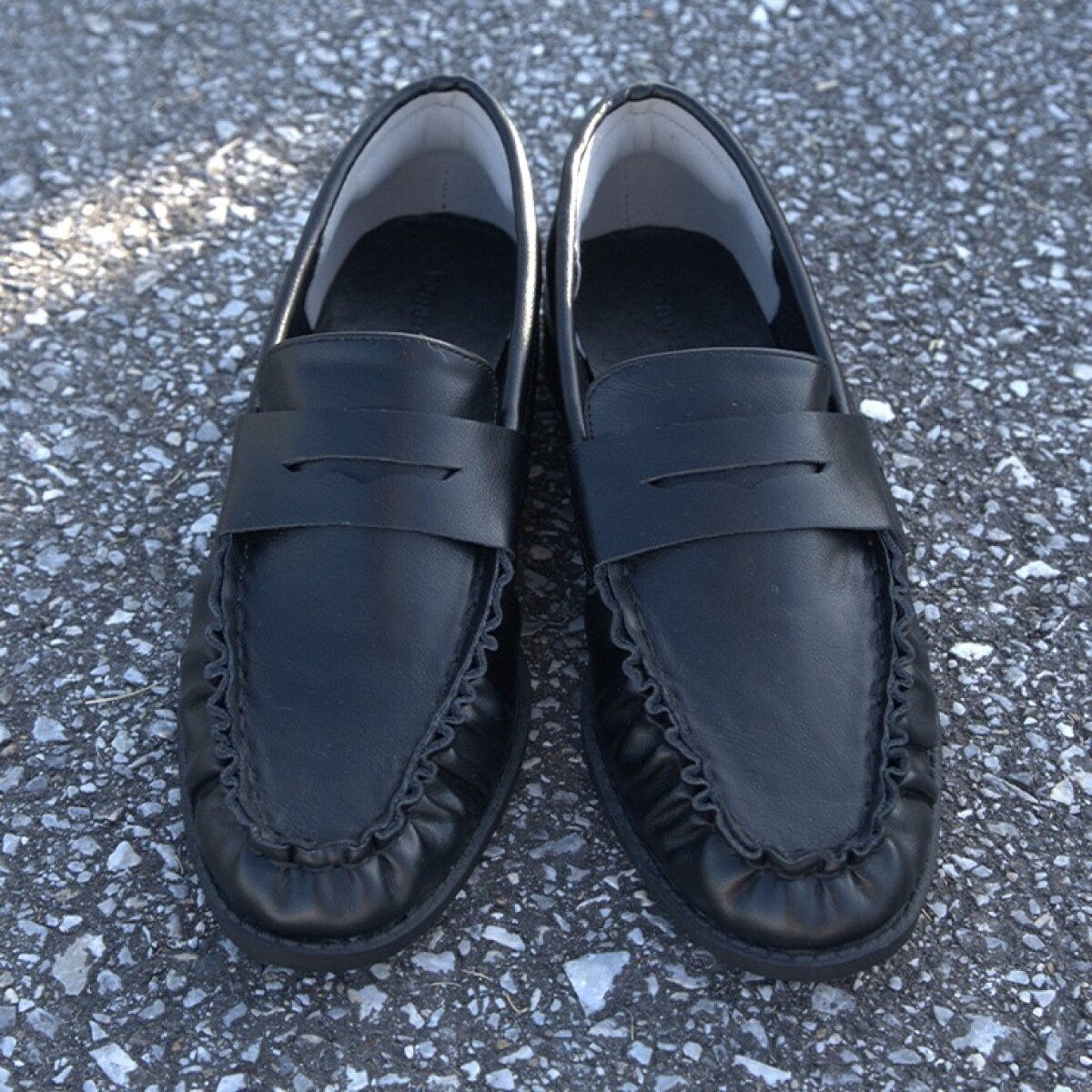 黒いギャザーデザインのローファー。甲にシンプルなベルト飾りが付いている。