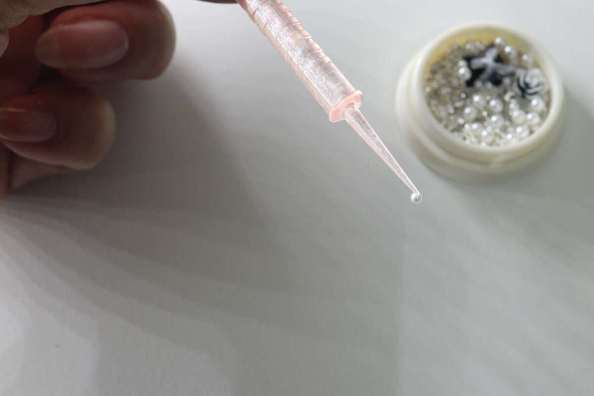 ネイル用スティックの細長い先端で小さなパールパーツを拾う