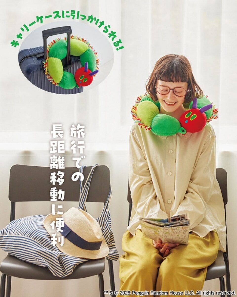 はらぺこあおむしを模したネックピローを首に着けて、笑顔で本を読む女性