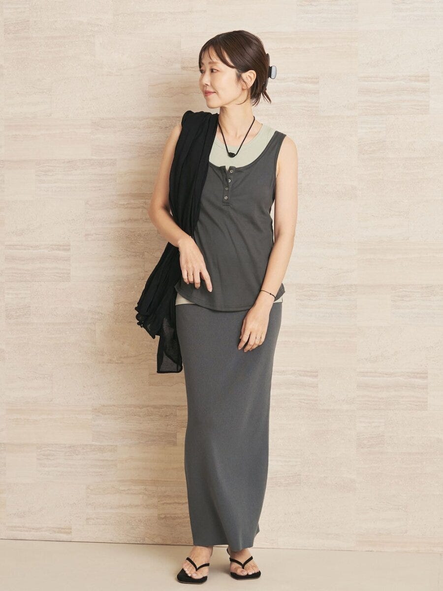 グレーのニットタンクとロングスカートのセットアップを着た女性が黒いストールを肩にかけている