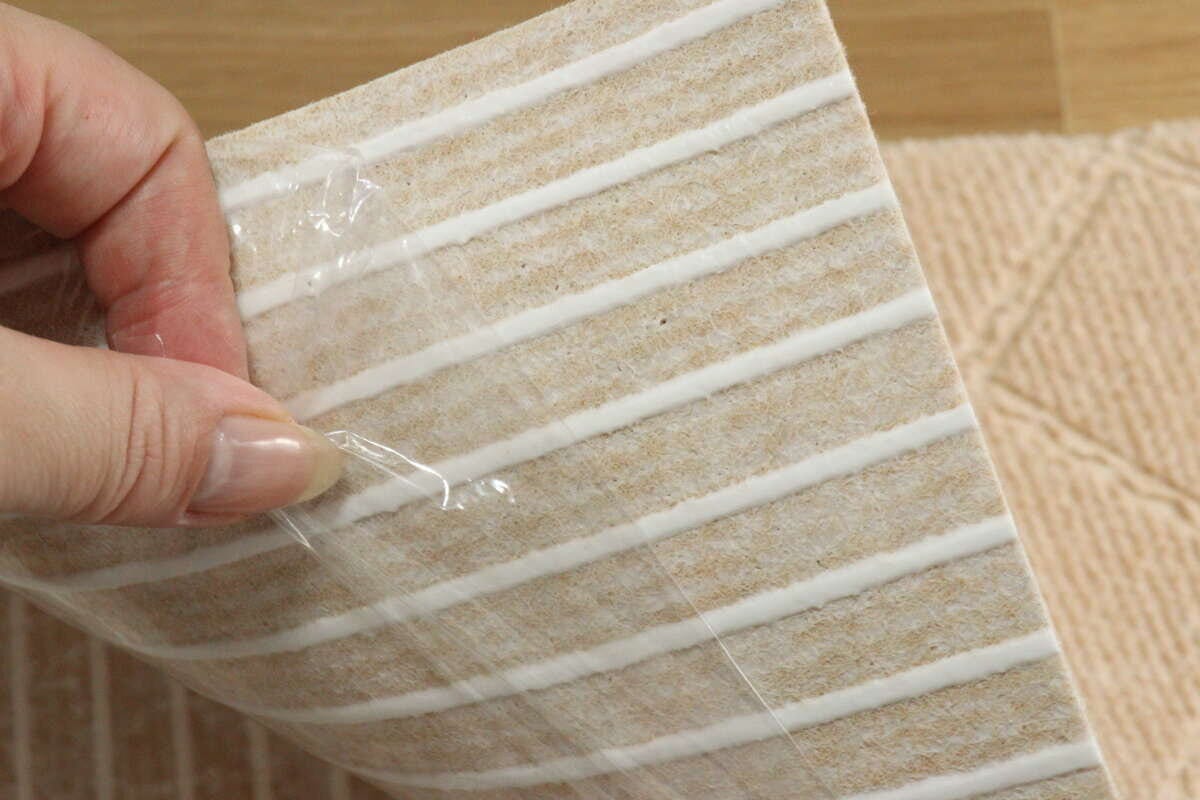 女性の指が吸着マットの裏面の保護フィルムを剥がしているクローズアップ
