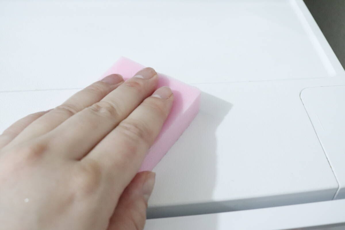 ピンクのメラミンスポンジで冷蔵庫上を掃除する手