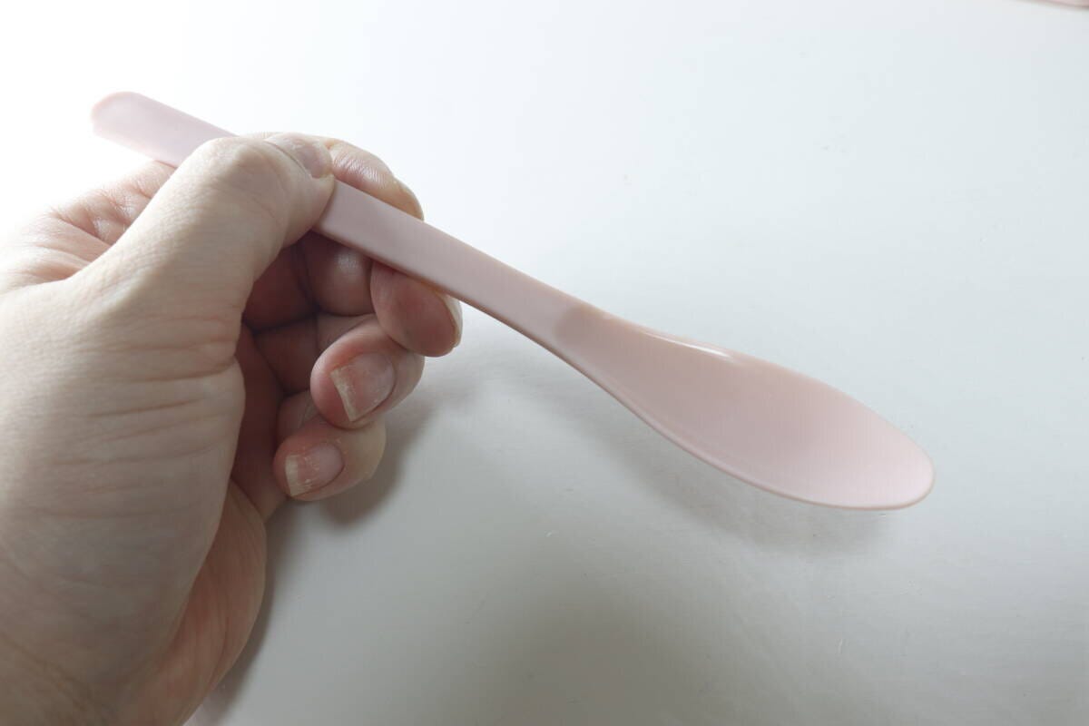 右手がピンク色のスプーンを持ち、細身でなめらかな縁が見える
