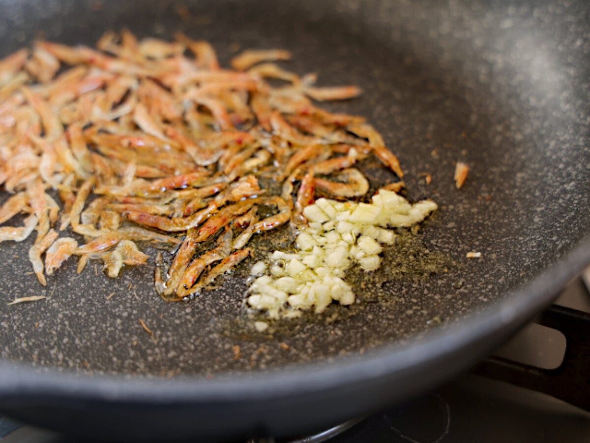 フライパンで乾燥桜海老とみじん切りにんにくをオリーブオイルで炒めている工程写真