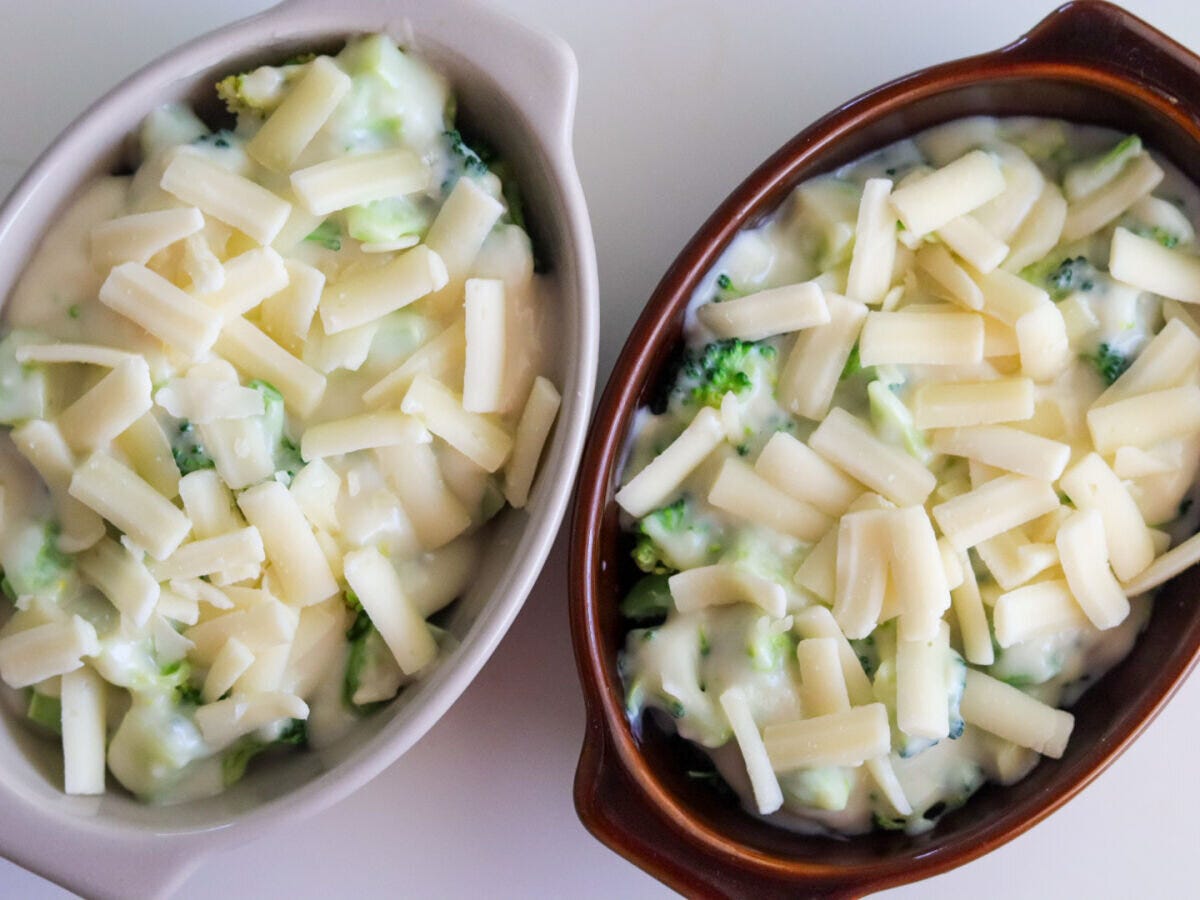 2つの耐熱グラタン皿にブロッコリーとクリームソースを入れてピザ用チーズをのせた焼く前の状態 2つの耐熱グラタン皿にブロッコリーとクリームソースを入れてピザ用チーズをのせた焼く前の状態