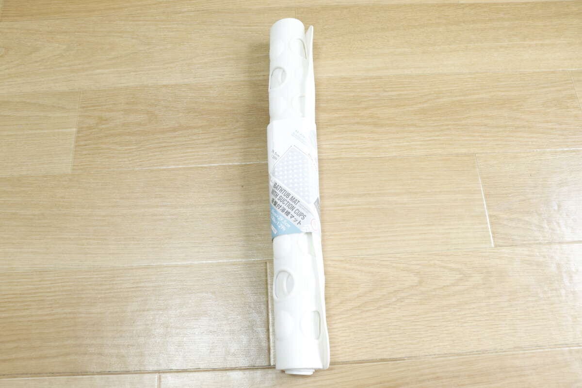 木目の床に置かれた、ロール状に巻かれた白い吸盤付浴槽マット