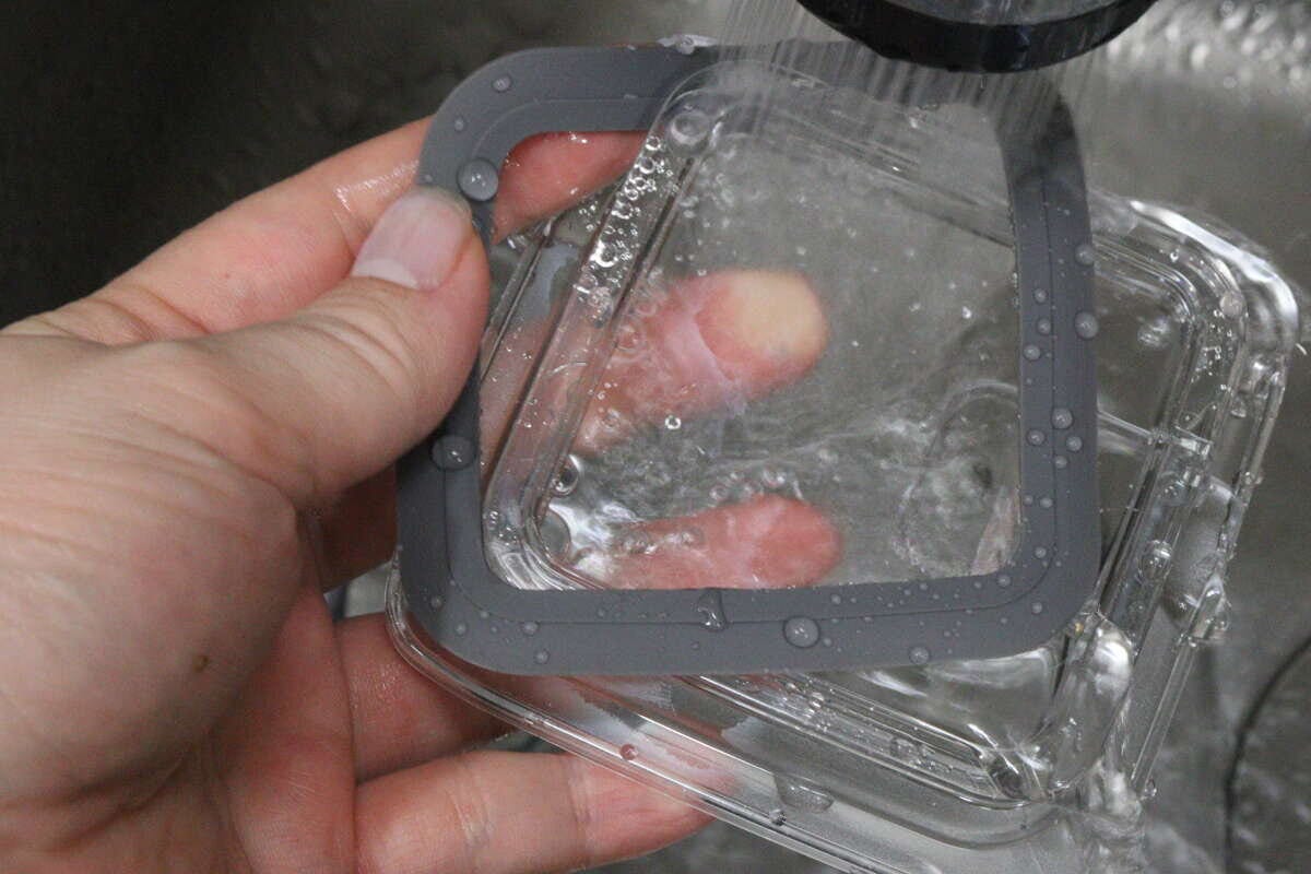 女性の手が持っている密閉容器のフタに、シャワーから水が勢いよくかかっている様子 女性の手が持っている密閉容器のフタに、シャワーから水が勢いよくかかっている様子