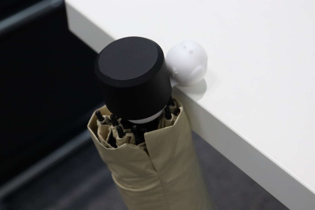 折りたたみ傘が白いテーブルの角に置かれ、シマエナガ型ストッパーで固定されている
