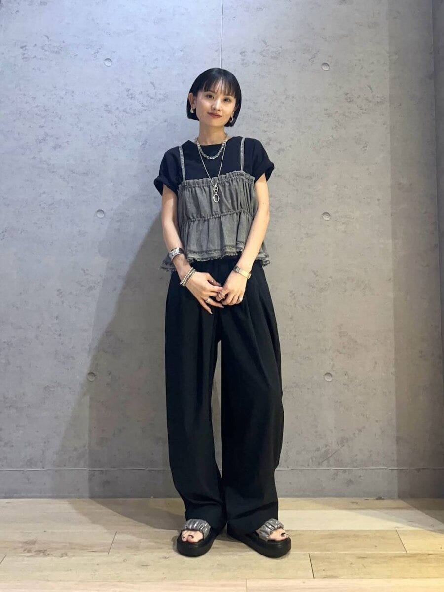 黒Tと黒ワイドパンツにデニムビスチェを重ね着した女性