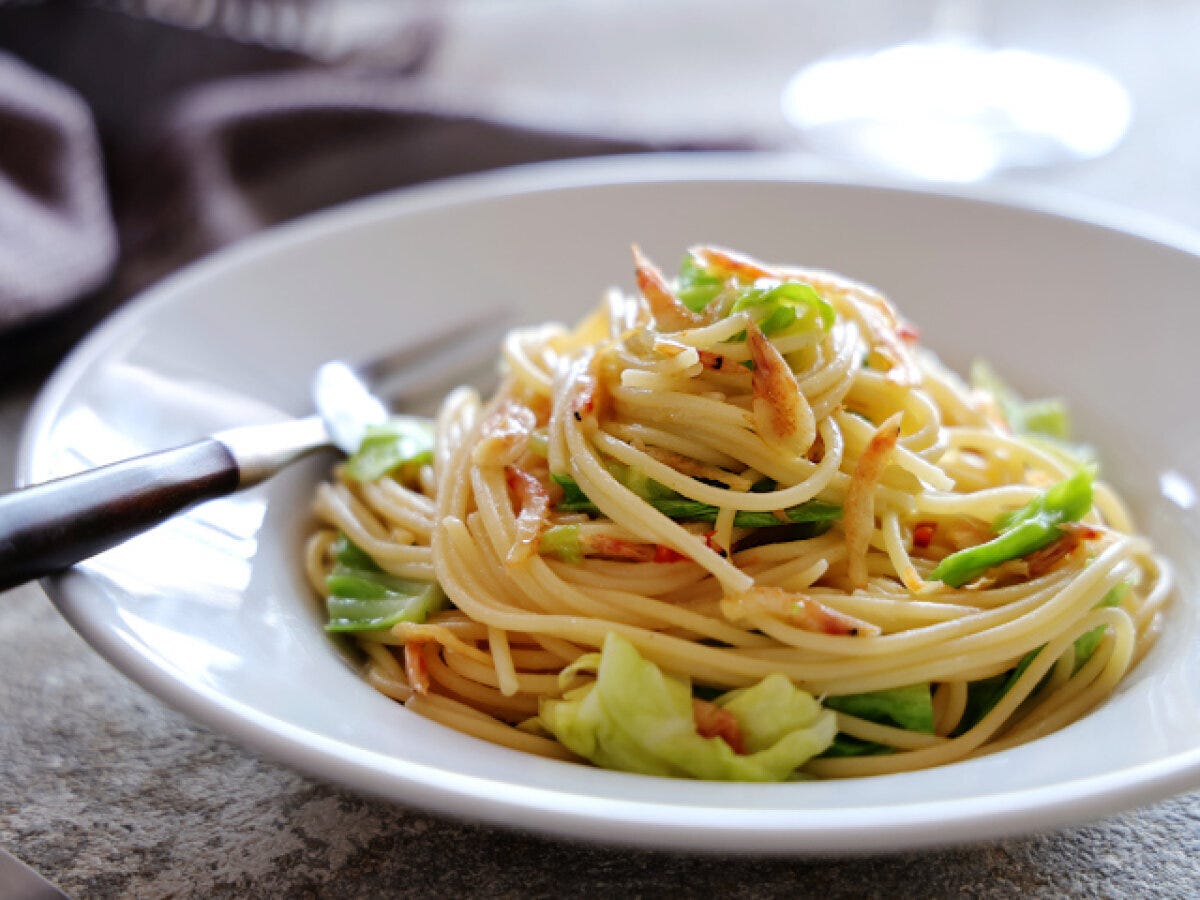 白い皿に盛られた春キャベツと桜海老のスパゲッティにフォークが刺さった完成品の俯瞰写真