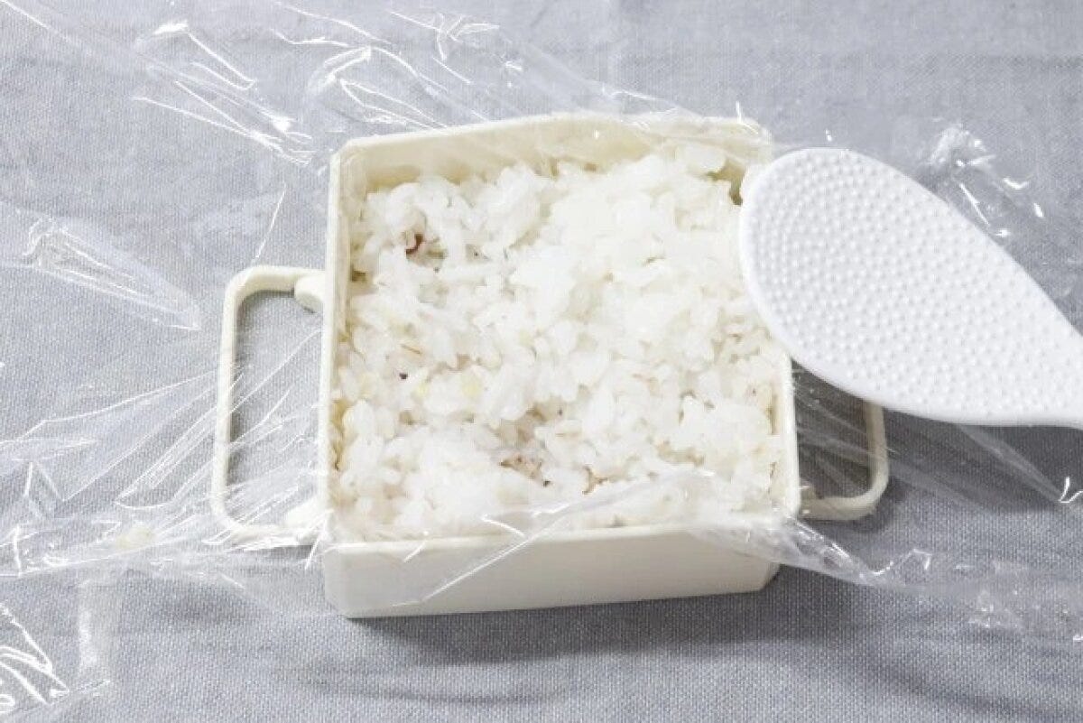 白いご飯冷凍保存型にラップを敷き、ご飯を入れ、しゃもじが添えられている 白いご飯冷凍保存型にラップを敷き、ご飯を入れ、しゃもじが添えられている