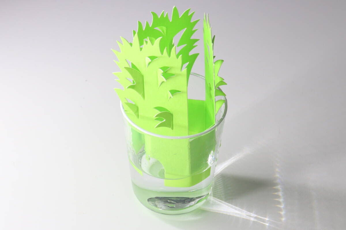 組み立てた緑色のペーパー加湿器を水が入った透明なグラスに差し込んでいる 組み立てた緑色のペーパー加湿器を水が入った透明なグラスに差し込んでいる