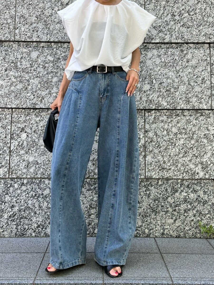 白いギャザーブラウスとワイドデニムを着用し、黒いバッグを持つ女性の全身