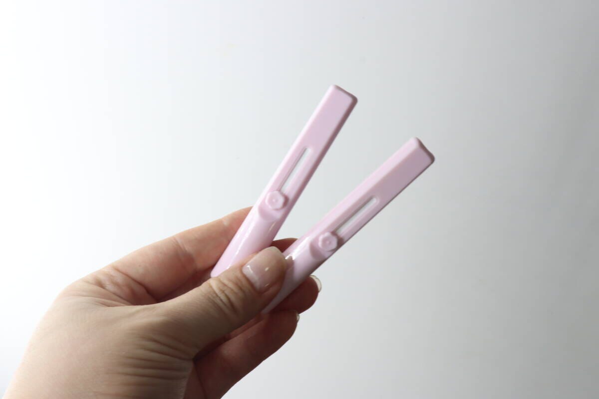 女性がピンク色のスライド式メイクブラシ2本を指で挟んで持っている 女性がピンク色のスライド式メイクブラシ2本を指で挟んで持っている