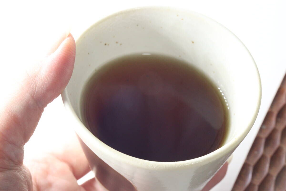 女性がやきいも茶の入った湯呑み茶碗を持ち上から覗き込んでいる 女性がやきいも茶の入った湯呑み茶碗を持ち上から覗き込んでいる