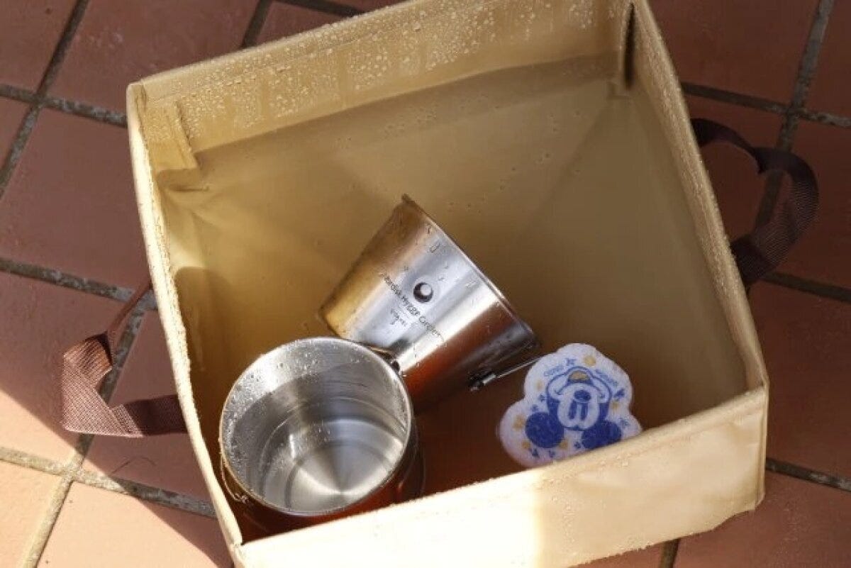 水と食器が入ったベージュ色の折りたたみキャンプバケツ