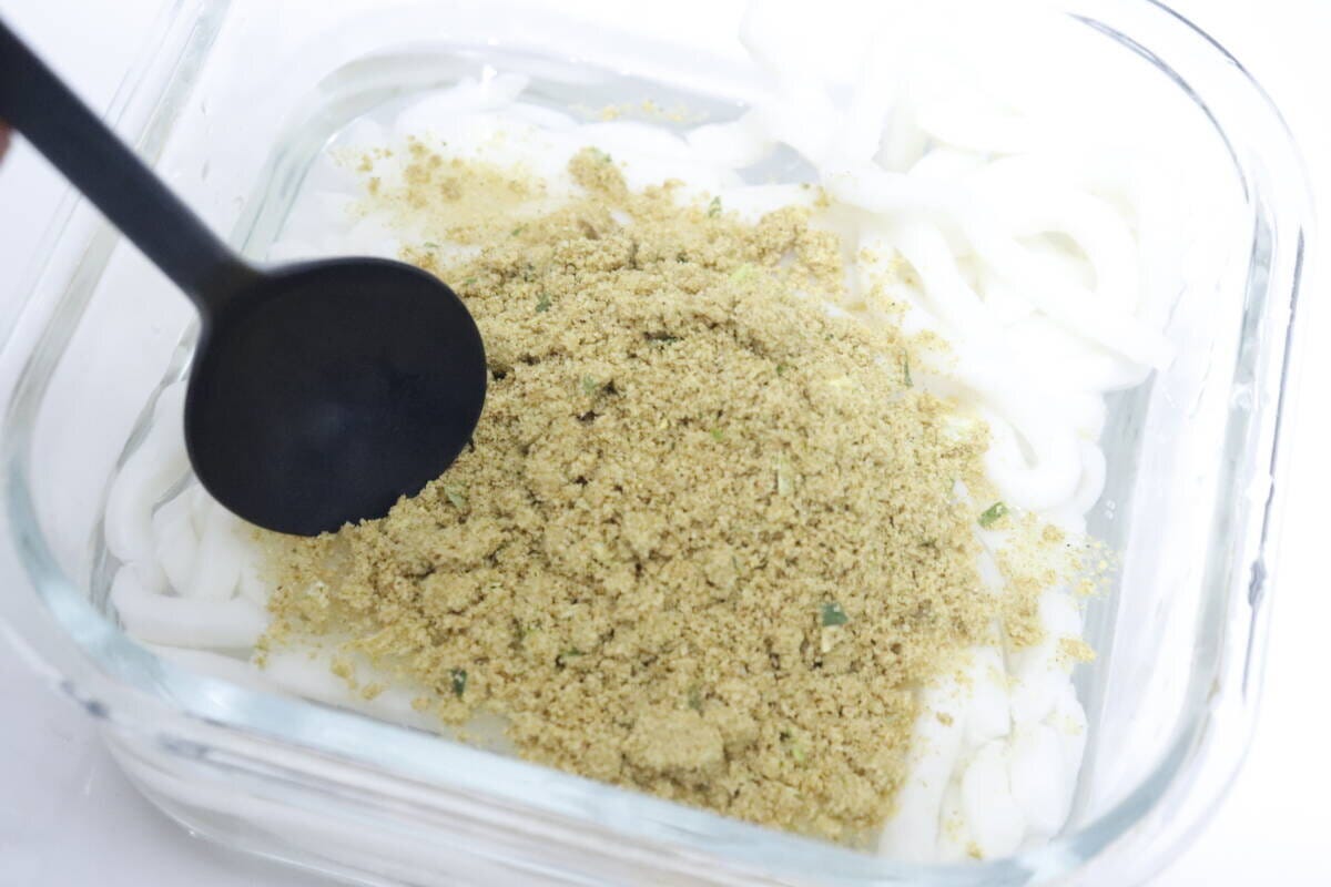 透明な耐熱容器に入れたうどん麺に粉末スープを入れ、スプーンを添えている 透明な耐熱容器に入れたうどん麺に粉末スープを入れ、スプーンを添えている