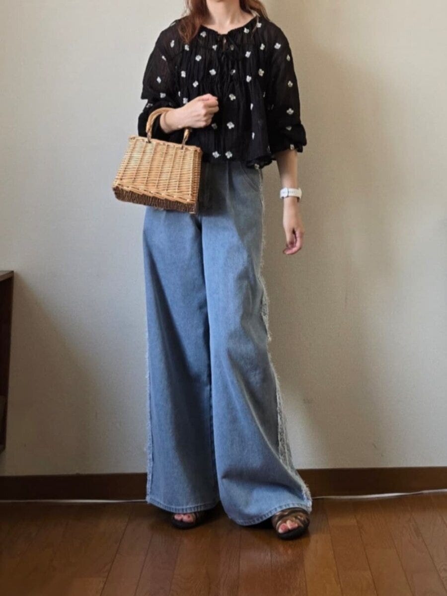 花柄黒ブラウスとライトブルーのワイドデニム、カゴバッグを持つ女性 花柄黒ブラウスとライトブルーのワイドデニム、カゴバッグを持つ女性