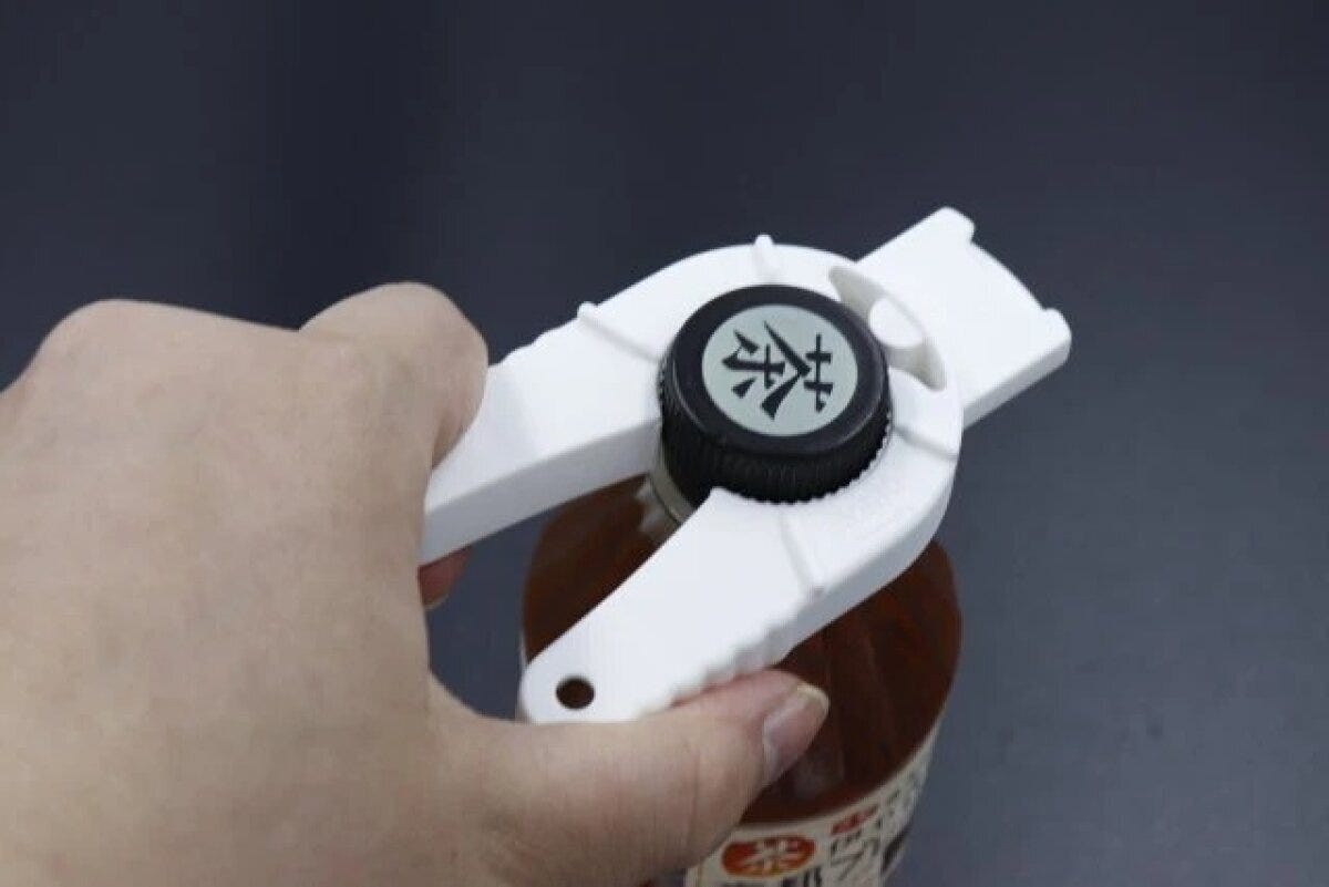 白い多機能オープナーで茶色い液体の入った瓶の黒いキャップを回している手元 白い多機能オープナーで茶色い液体の入った瓶の黒いキャップを回している手元