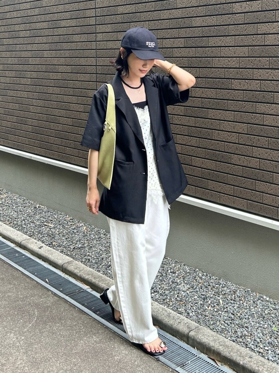 黒の半袖ジャケットと白ワイドパンツ、キャップを被った女性が歩いている。