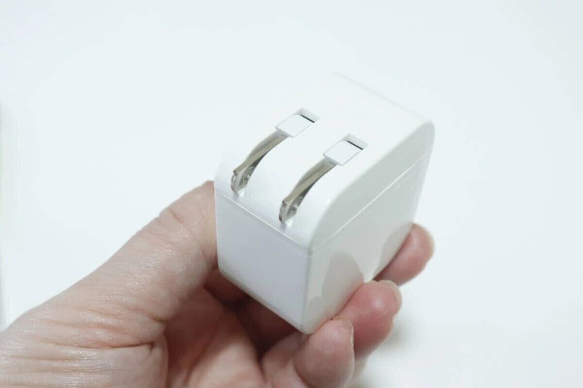 白いUSB充電器のプラグ部分が折りたたまれている様子を手に持っている 白いUSB充電器のプラグ部分が折りたたまれている様子を手に持っている