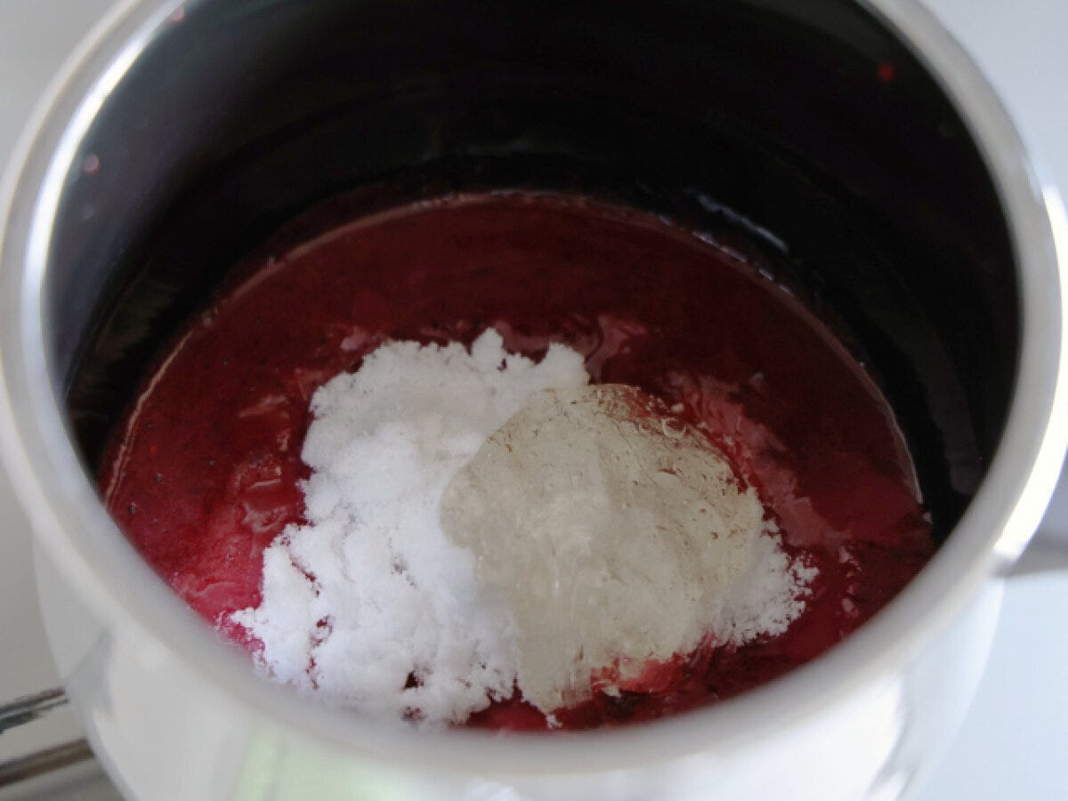 ベリーピューレに上白糖と水あめを加える工程 ミックスベリーピューレが入った鍋に白い上白糖と透明な水あめを加えた俯瞰写真