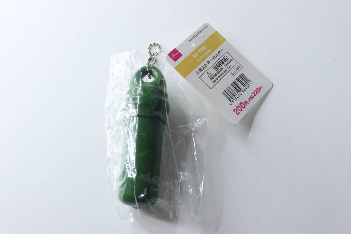 緑色の筒状の小物入れキーホルダーが透明な袋に入っている。商品タグも見える