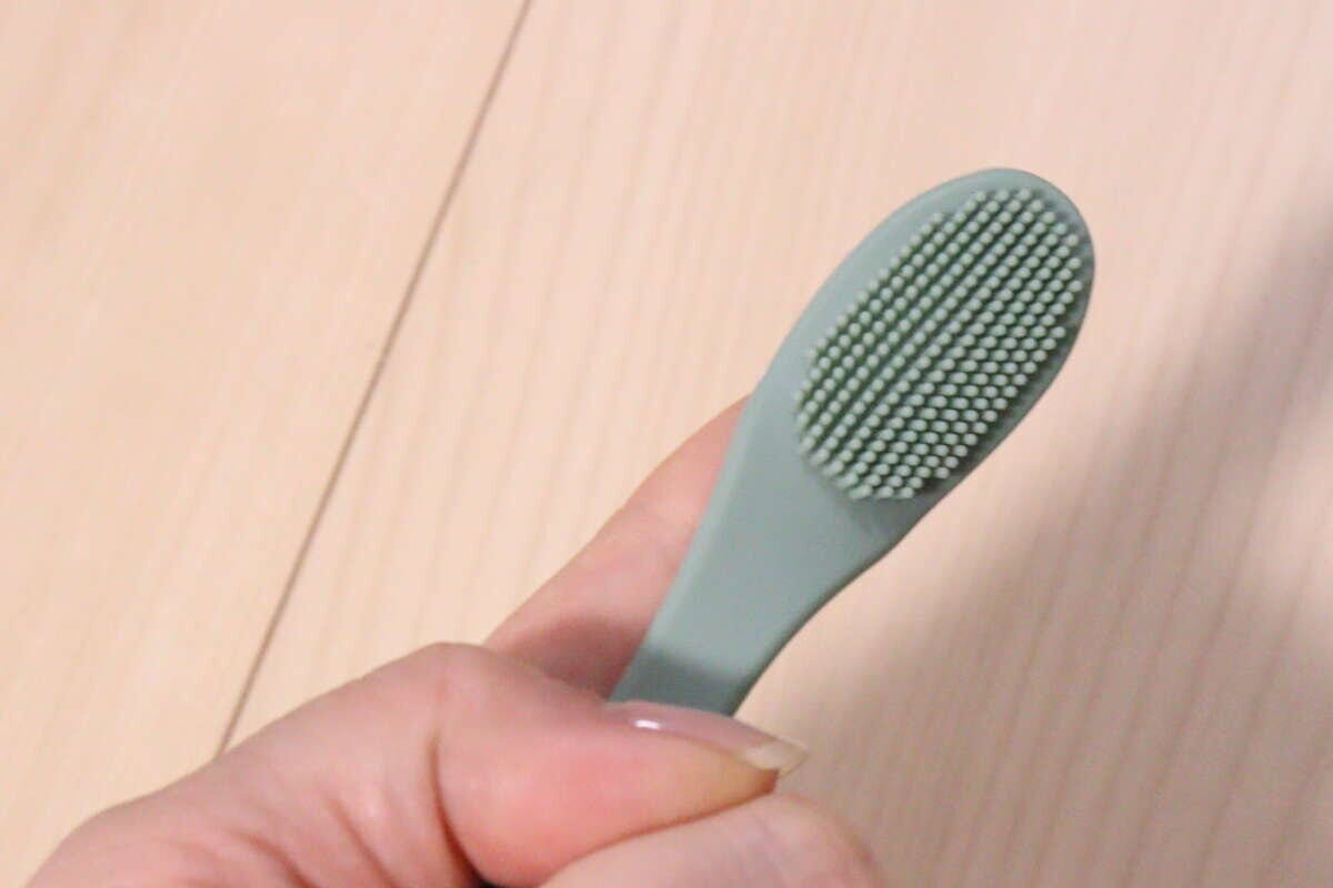 人差し指に薄い緑色のやわらかいペット用ブラシをはめている手元 人差し指に薄い緑色のやわらかいペット用ブラシをはめている手元