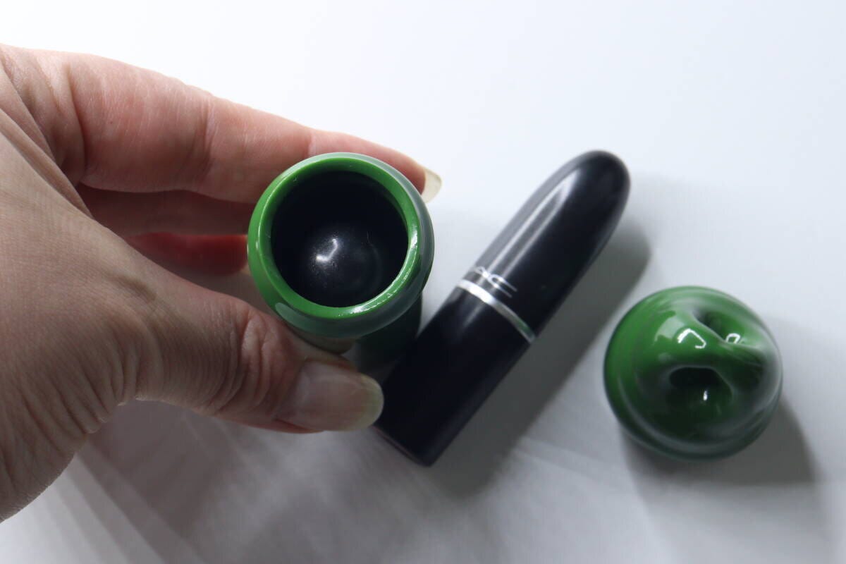 女性の手が緑色の小物入れキーホルダーの本体を持ち、その横に黒い口紅が置かれている
