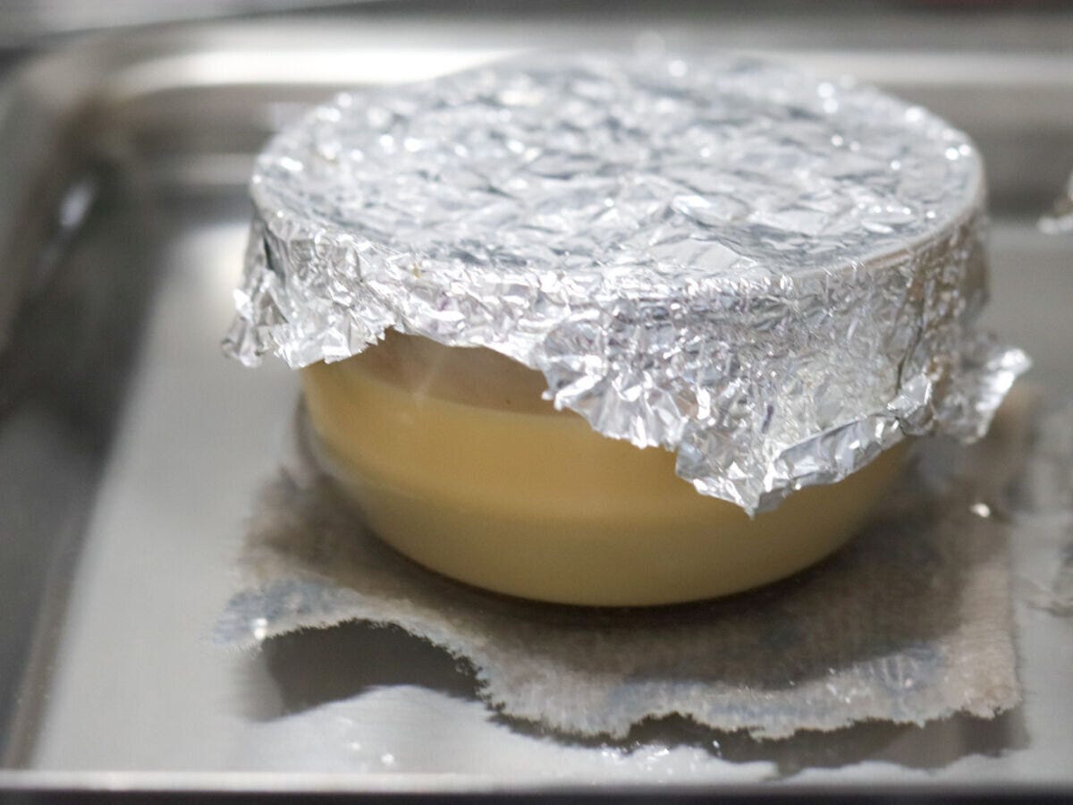 布巾を敷いたバットに湯を張りアルミホイルで蓋をしたプリンカップを湯煎焼きしている様子