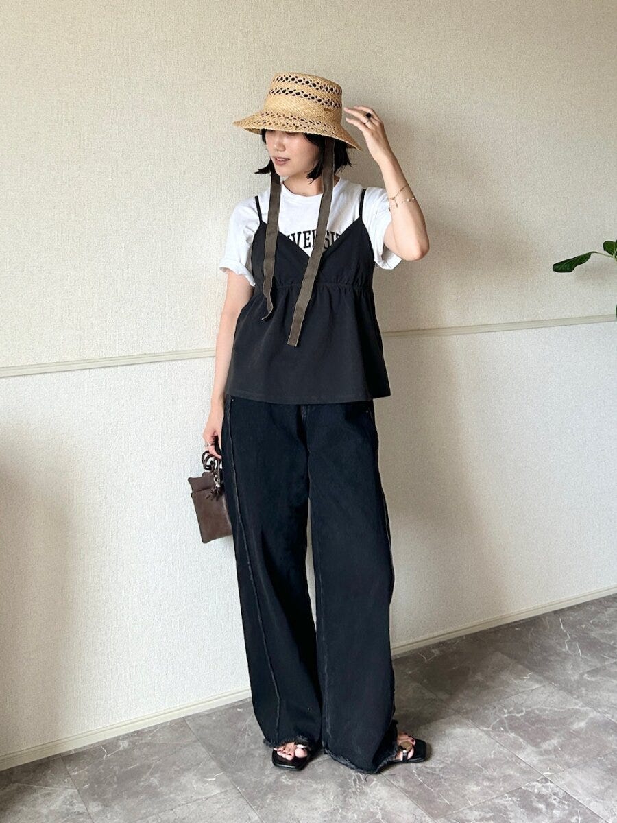 白Tと黒キャミ重ね着、黒ワイドパンツの女性が麦わら帽子を被り立つ