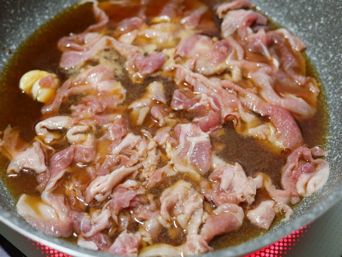 煮汁が入ったフライパンに豚こま切れ肉が加えられ、ほぐされている様子 煮汁が入ったフライパンに豚こま切れ肉が加えられ、ほぐされている様子