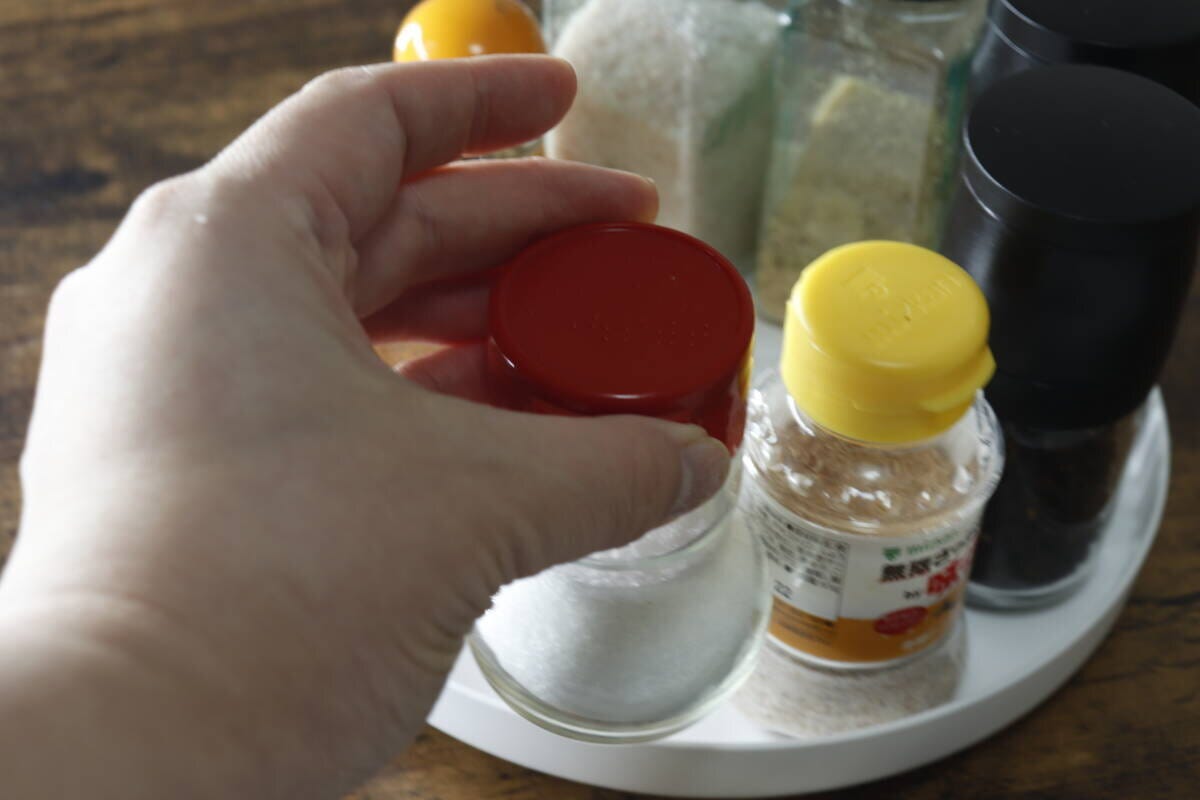 白い回転式物置トレーに置かれた調味料ボトルを、片手で掴んで取り出している様子