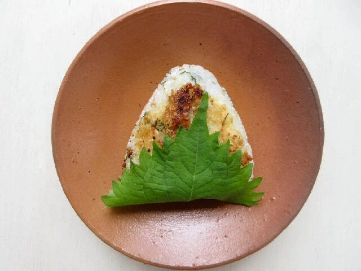 大葉と胡麻のみそ焼きおにぎり1個が焦げ目がつき、大葉に包まれて茶色の皿に盛られている