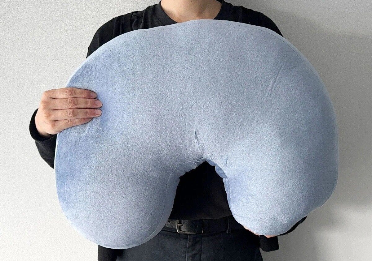 青いU字型クッションを両手で抱えている男性