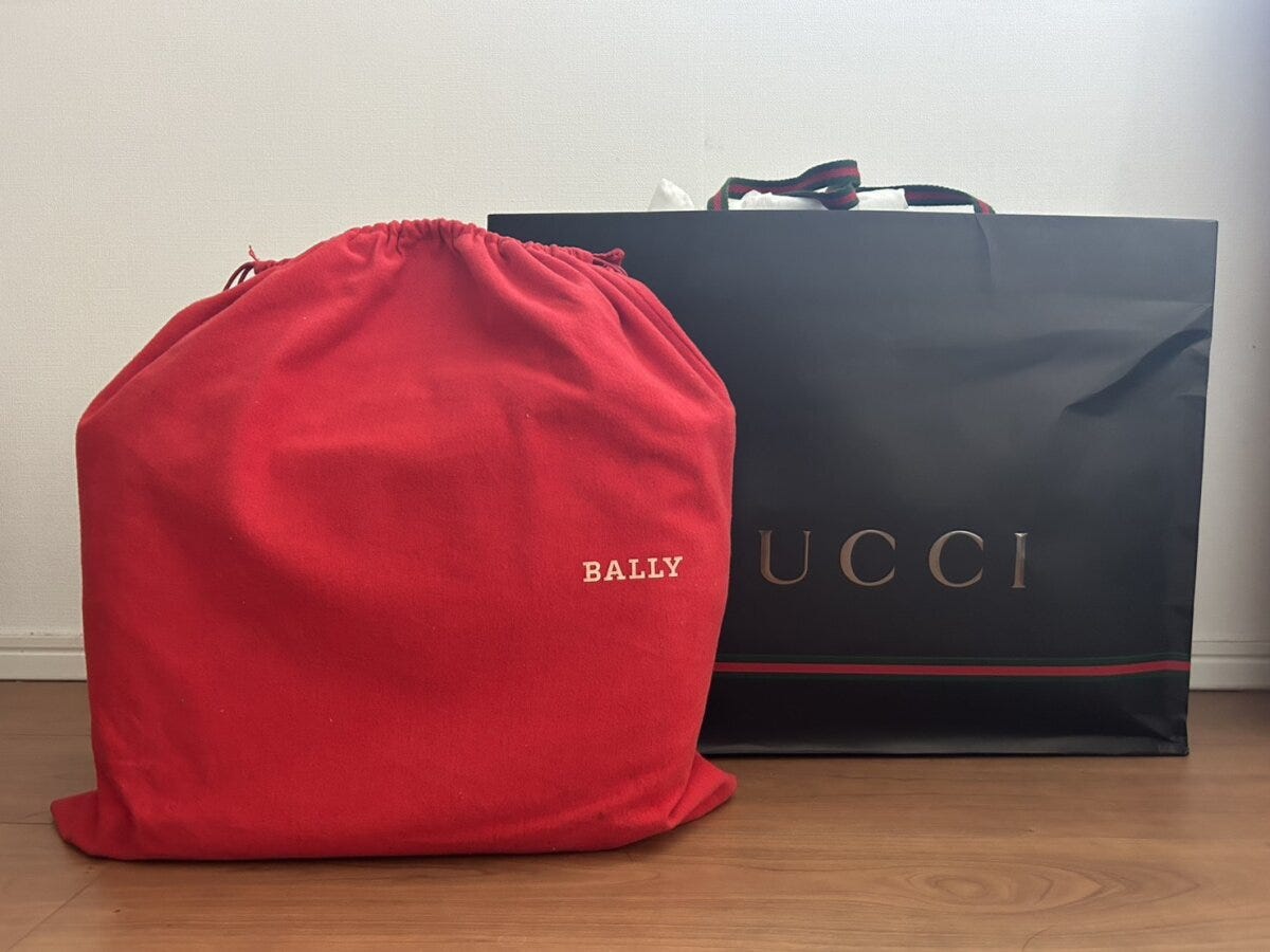 床に置かれたBALLYの赤い巾着保存袋とGUCCIの黒いショッピングバッグ
