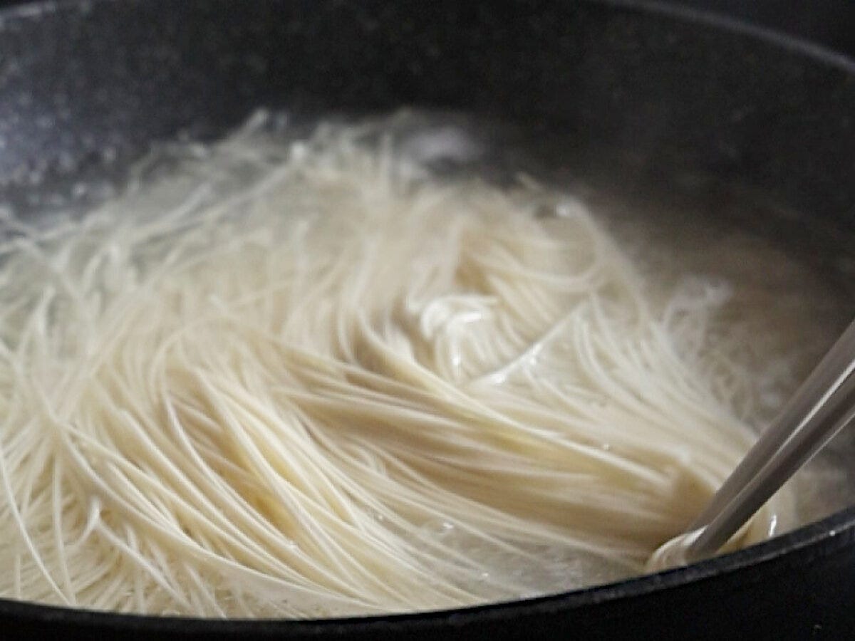 黒い鍋でそうめんが茹でられており、箸で麺をほぐしている様子。 黒い鍋でそうめんが茹でられており、箸で麺をほぐしている様子。