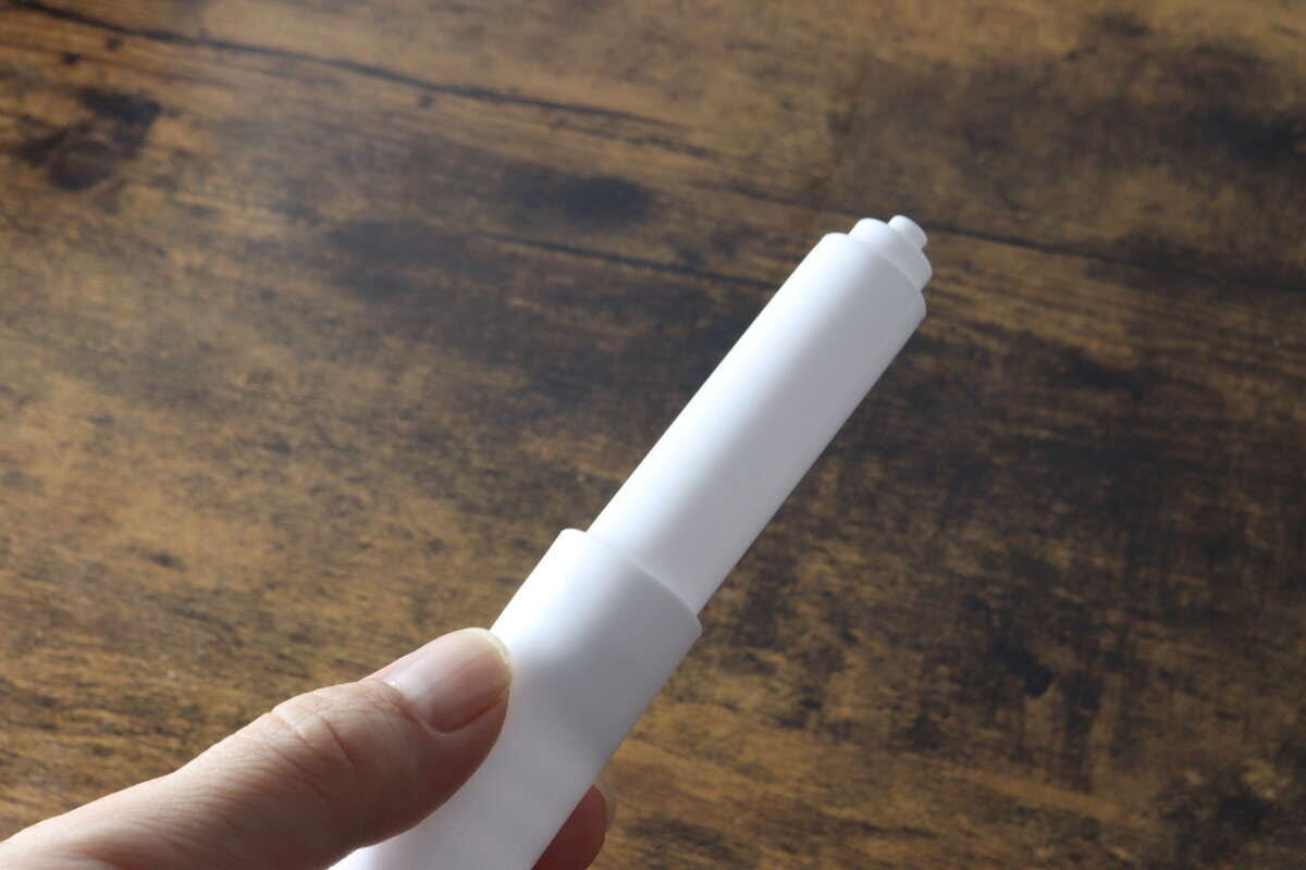 女性の手が白いトイレットペーパー替え芯ホルダーを横向きに持っている 女性の手が白いトイレットペーパー替え芯ホルダーを横向きに持っている