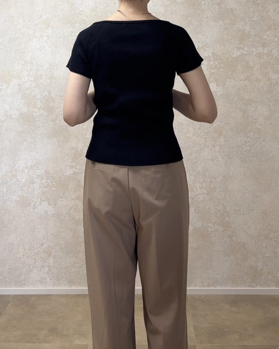 黒いリブカーディガンとベージュのワイドパンツを着用した女性が後ろ向きに立っている