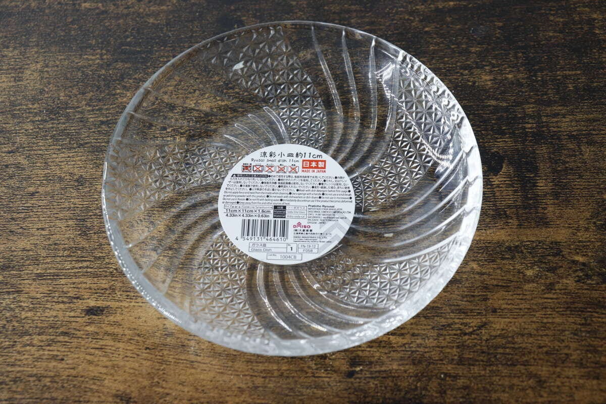 木目のテーブルに置かれたガラス小皿の裏面に商品情報シールが貼られている俯瞰写真 木目のテーブルに置かれたガラス小皿の裏面に商品情報シールが貼られている俯瞰写真