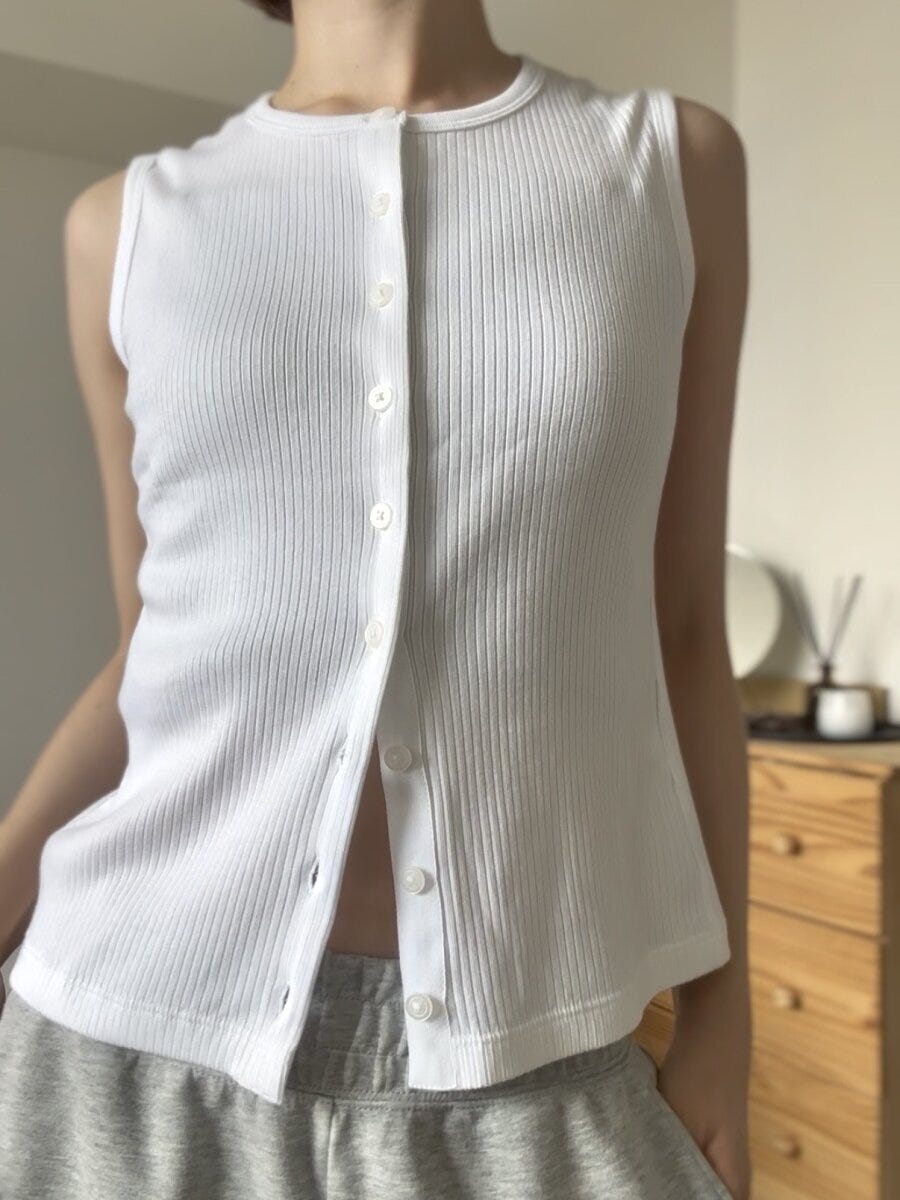 白いリブノースリーブを着た女性の胸元アップ、ボタンを数個開けている