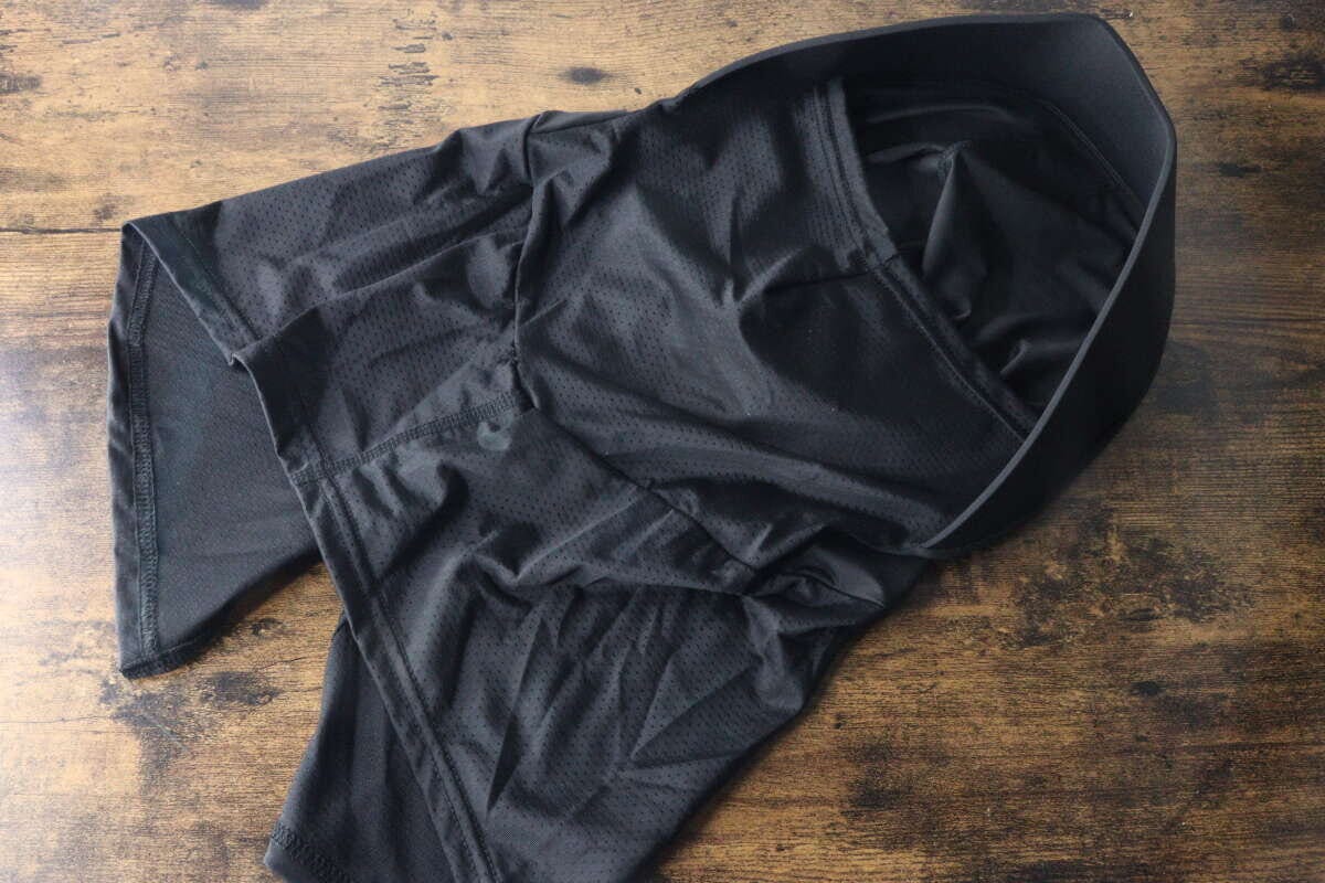 黒いフェイスガードが広げられて木目のテーブルに置かれている。メッシュ素材の通気性がわかる 黒いフェイスガードが広げられて木目のテーブルに置かれている。メッシュ素材の通気性がわかる