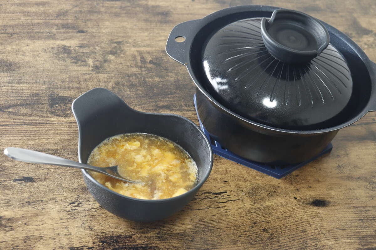 雑炊が入ったダイソーの黒い呑水と蓋付きの鍋が木製のテーブルに並んでいる